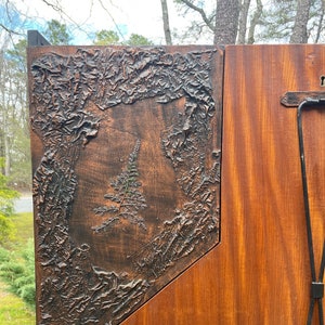 May include: A wooden cabinet with a textured copper panel featuring a fern design. The cabinet has a dark wood finish and a black metal frame.
