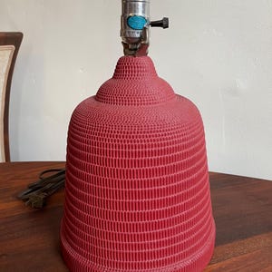 K&ouml;nnte beinhalten: Eine rote Lampenbasis mit einem strukturierten, gerippten Design. Die Lampenbasis hat eine Metallfassung und ein Kabel.
