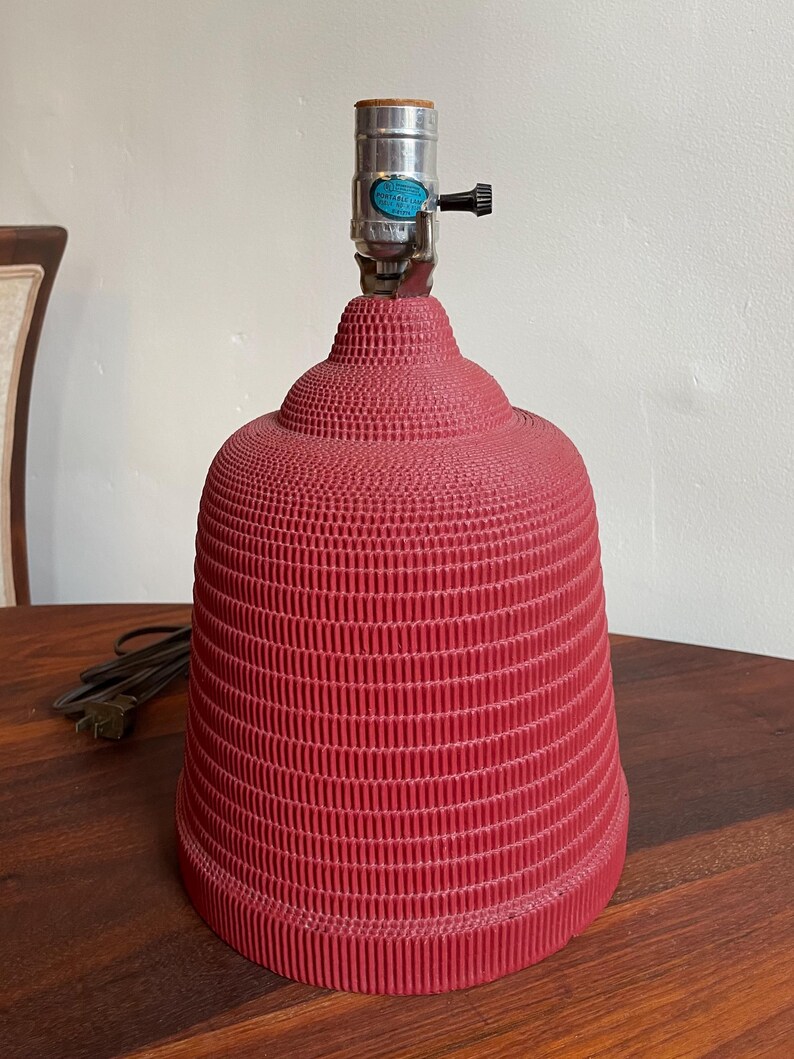 K&ouml;nnte beinhalten: Eine rote Lampenbasis mit einem strukturierten, gerippten Design. Die Lampenbasis hat eine Metallfassung und ein Kabel.