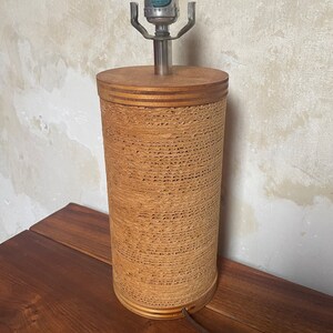 May include: A brown lamp with a woven cylindrical base and a silver metal lampshade. The lamp has a black cord and plug.