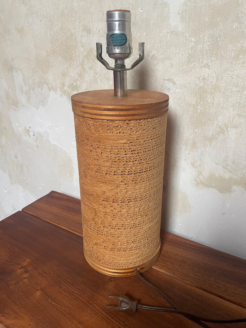 May include: A brown lamp with a woven cylindrical base and a silver metal lampshade. The lamp has a black cord and plug.