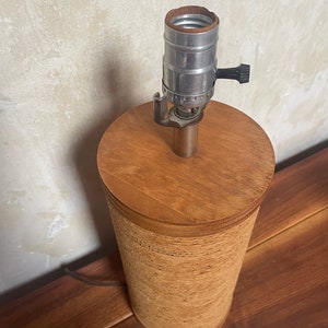 May include: A brown lamp base with a woven texture and a silver lamp socket with a black knob.