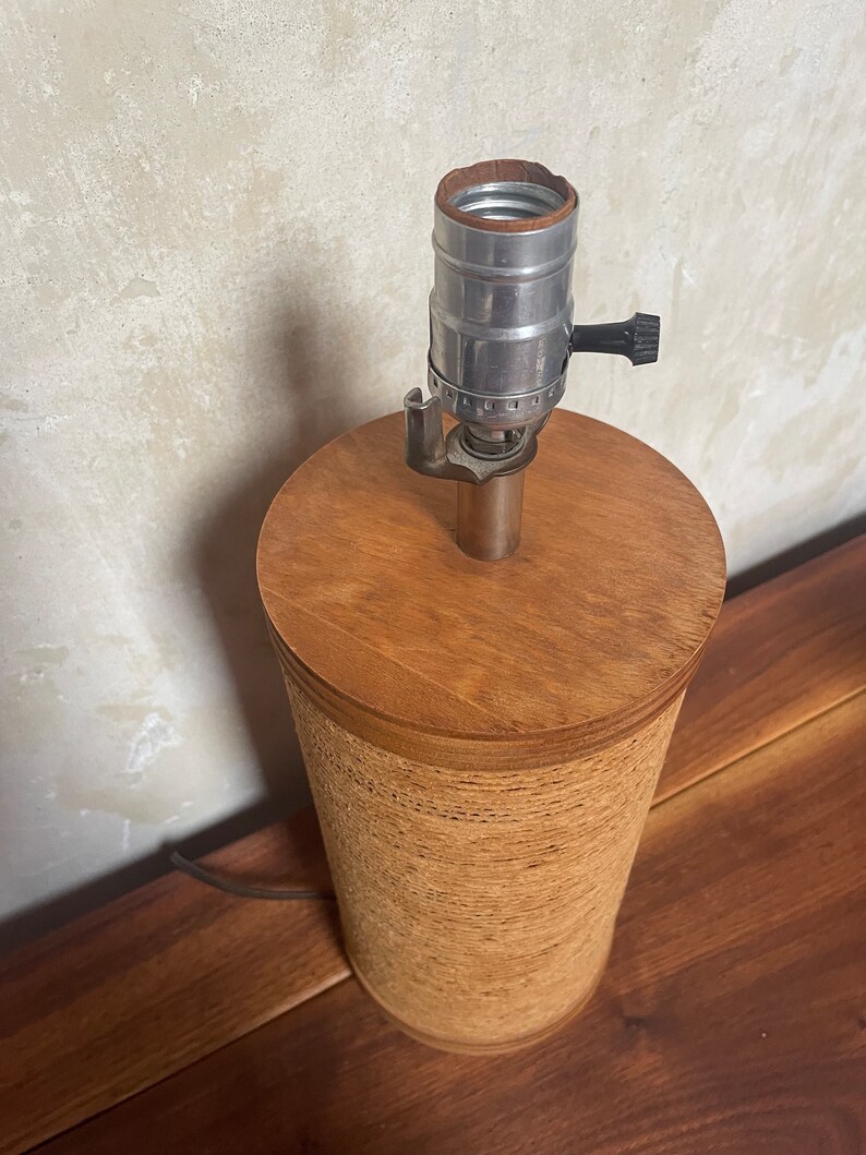 May include: A brown lamp base with a woven texture and a silver lamp socket with a black knob.