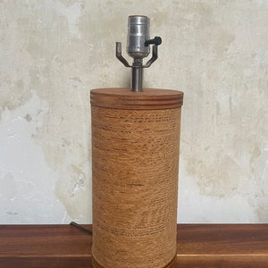May include: A brown cylindrical lamp base with a woven texture and a silver lamp socket. The lamp base has a wooden top and bottom.