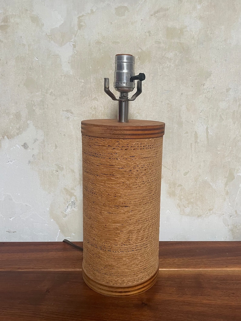 May include: A brown cylindrical lamp base with a woven texture and a silver lamp socket. The lamp base has a wooden top and bottom.