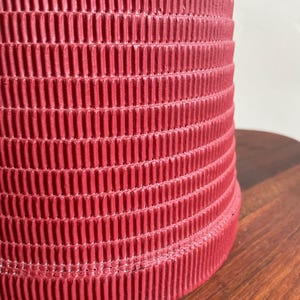 K&ouml;nnte beinhalten: Eine rote Pappe mit einer gerippten Textur. Die R&ouml;hre ist zylindrisch und hat eine glatte, abgerundete Kante.