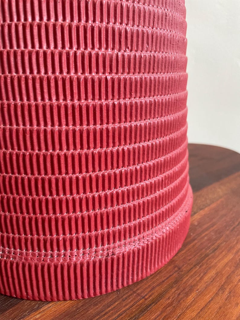 K&ouml;nnte beinhalten: Eine rote Pappe mit einer gerippten Textur. Die R&ouml;hre ist zylindrisch und hat eine glatte, abgerundete Kante.