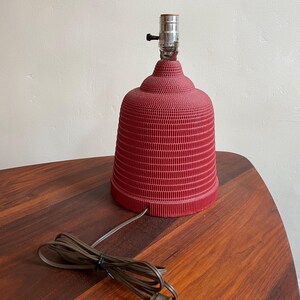K&ouml;nnte beinhalten: Eine rote Keramik-Tischlampe mit einem strukturierten, gerippten Design. Die Lampe hat eine schlichte, klassische Form und ein braunes Kabel.