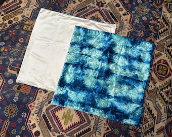 Könnte beinhalten: Zwei rechteckige Kissenbezüge. Einer ist einfarbig cremeweiß, der andere hat ein blau-türkises Batikmuster. Sie sind aus weichem, strukturiertem Stoff gefertigt und eignen sich zur Dekoration.