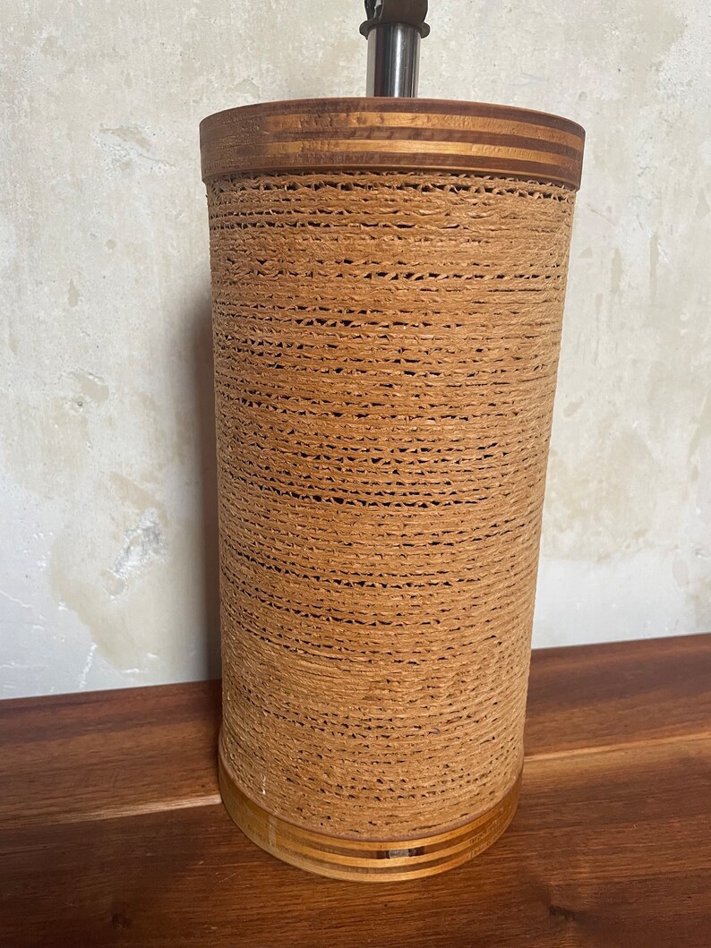 May include: A brown woven lamp base with a wooden top and bottom. The base is made of a woven material that looks like rope.