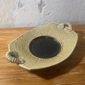May include: A light green ceramic serving tray with two handles. The tray has a textured surface and a dark brown center.