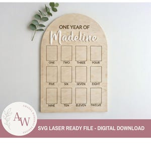 Könnte beinhalten: Eine Meilensteintafel aus Holz mit dem Text "ONE YEAR OF Madeline" in Weiß. Die Tafel hat zwölf rechteckige Felder, die mit den Zahlen eins bis zwölf beschriftet sind. Der untere Teil der Tafel lautet "SVG LASER READY FILE - DIGITAL DOWNLOAD".