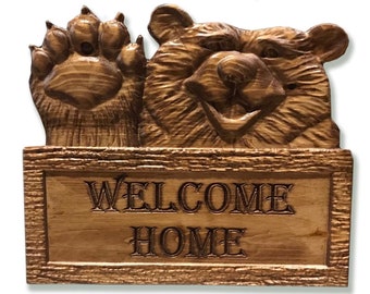 May include: A wooden carved bear with a paw raised in the air, peeking over a wooden sign that reads "WELCOME HOME".