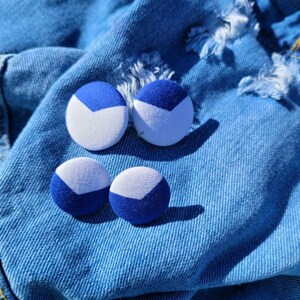 May include: Four round, fabric-covered buttons with a blue and white color block design. The buttons are arranged on a blue denim background. The buttons have a white chevron shape on a blue background.
