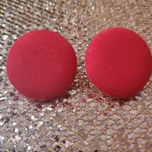 May include: A pair of red fabric earrings. The earrings are round and have a smooth texture.