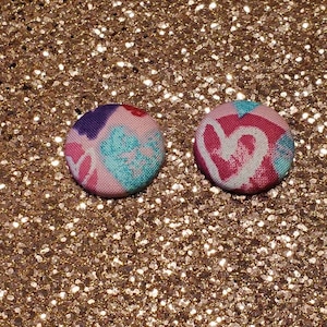 Puede incluir: Un par de pendientes de botón de tela rosa con un patrón de corazón colorido.
