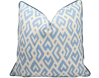 May include: A square throw pillow featuring a light blue and off-white geometric pattern of interlocking diamond shapes. The pillow is finished with a dark blue piped edge trim that outlines the entire perimeter of the square cushion cover.