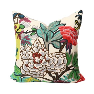 K&ouml;nnte beinhalten: Ein Dekokissen mit einem floralen Muster mit gro&szlig;en wei&szlig;en Bl&uuml;ten, gr&uuml;nen Bl&auml;ttern und roten, rosa und gelben Akzenten. Das Kissen ist aus einem weichen, wei&szlig;en Stoff gefertigt.