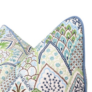 May include: A blue and green patterned pillow with embroidered details. The pillow has a light blue border and a white background.