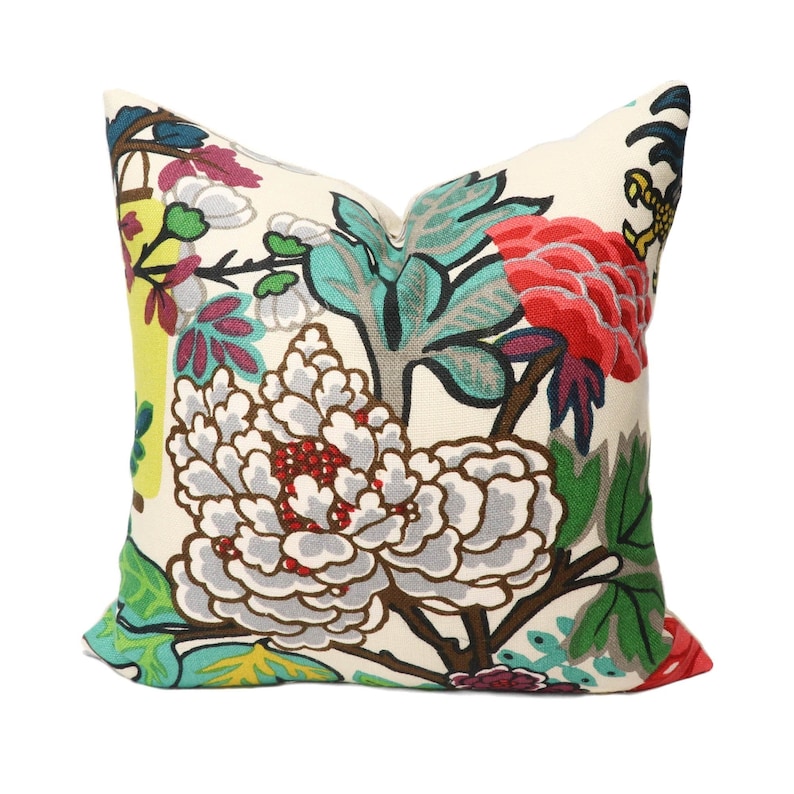 K&ouml;nnte beinhalten: Ein Dekokissen mit einem floralen Muster mit gro&szlig;en wei&szlig;en Bl&uuml;ten, gr&uuml;nen Bl&auml;ttern und roten, rosa und gelben Akzenten. Das Kissen ist aus einem weichen, wei&szlig;en Stoff gefertigt.