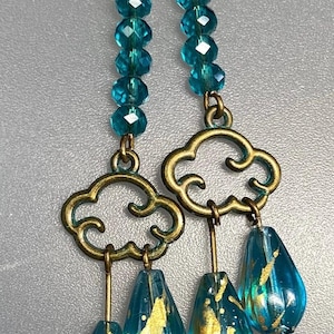 May include: Teal blue crystal bead dangle earrings with gold tone cloud charms and teardrop beads with gold flecks.