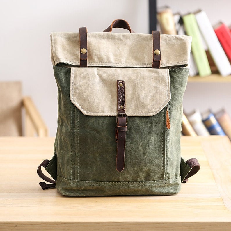 May include: A green and beige canvas backpack with brown leather straps and buckles. The backpack has a flap closure and a front pocket.