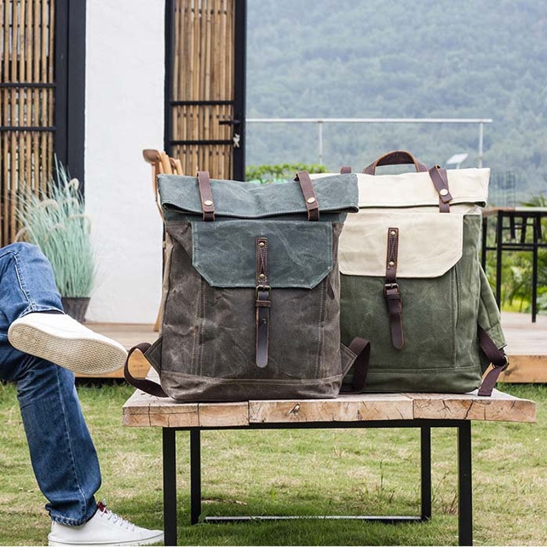 May include: Two canvas backpacks with leather straps and buckles. One backpack is green and brown, the other is white and green.