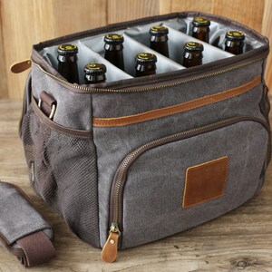 Puede incluir: Una bolsa de enfriador de lona gris con ribete de cuero marr&oacute;n y un bolsillo con cremallera. La bolsa de enfriador tiene una correa para el hombro y est&aacute; llena de seis botellas de vidrio marr&oacute;n.
