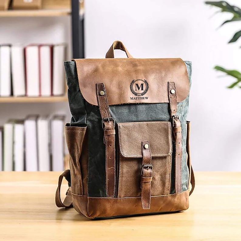 May include: A brown leather and canvas backpack with a large front pocket and a personalized leather patch with the initial "M" and the name "Matthew".