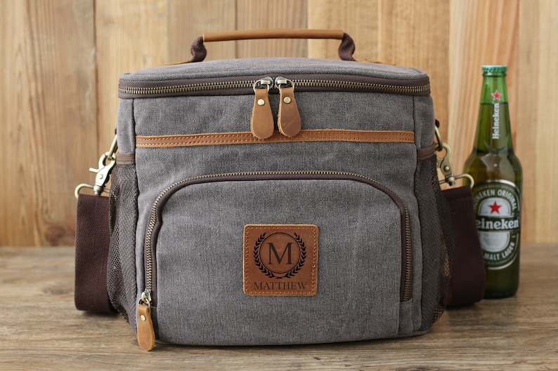 Puede incluir: Bolsa isot&eacute;rmica de lona gris con detalles en cuero marr&oacute;n y un parche personalizado con la inicial "M" y el nombre "MATTHEW".