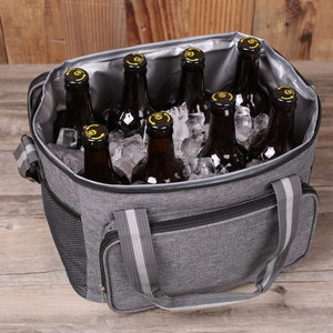 Op de afbeelding: Een grijze ge&iuml;soleerde koeltas met een ritssluiting en twee handvatten. De tas is gevuld met ijs en flessen bier.