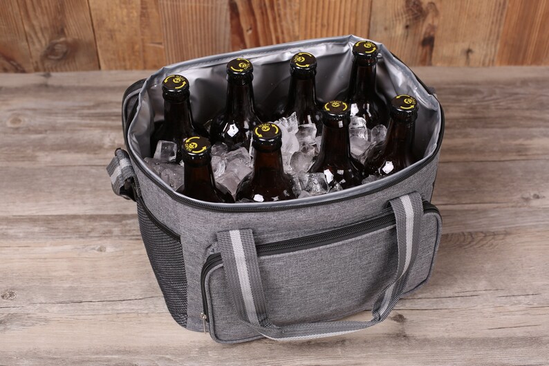 Op de afbeelding: Een grijze ge&iuml;soleerde koeltas met een ritssluiting en twee handvatten. De tas is gevuld met ijs en flessen bier.