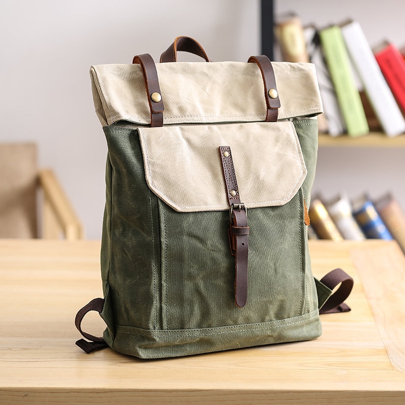 May include: A green and beige canvas backpack with brown leather straps and buckles. The backpack has a flap closure and a front pocket.