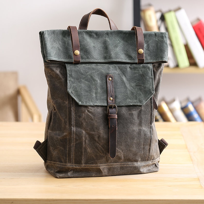 May include: A dark green canvas backpack with brown leather straps and buckles. The backpack has a flap closure and a front pocket.