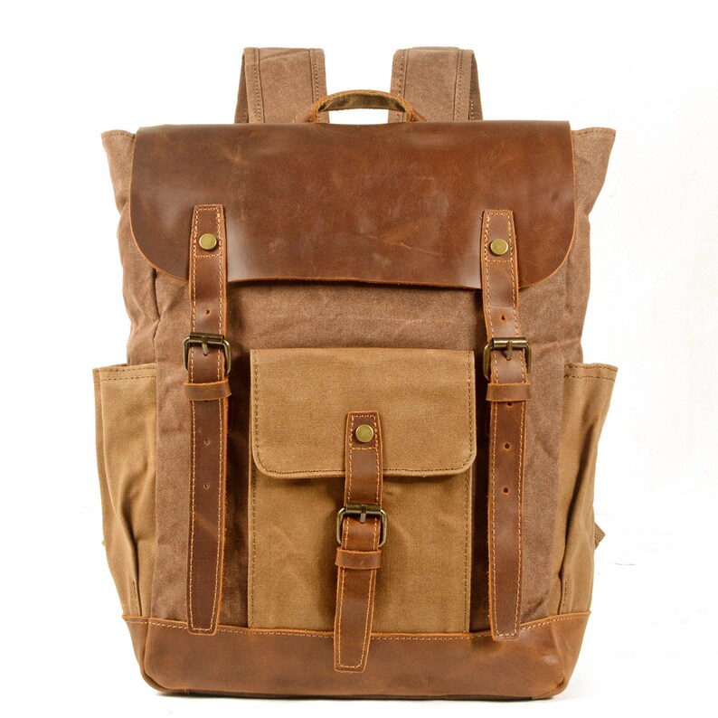 May include: A brown canvas backpack with leather accents and straps. The backpack has a large main compartment, a front pocket, and two side pockets. The backpack is made of durable materials and is perfect for everyday use.