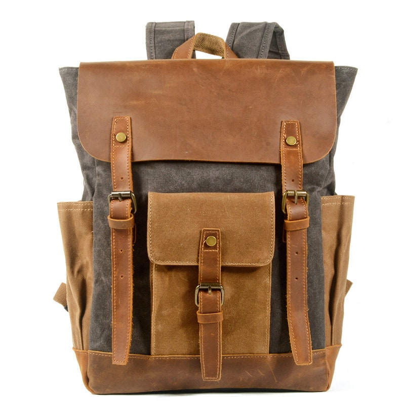 May include: A brown leather and canvas backpack with multiple pockets and buckles. The backpack has a gray canvas body with a brown leather flap and a brown canvas pocket on the front.