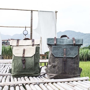 May include: Two canvas backpacks with leather straps and buckles. One backpack is green and the other is brown. Both backpacks have a flap closure.