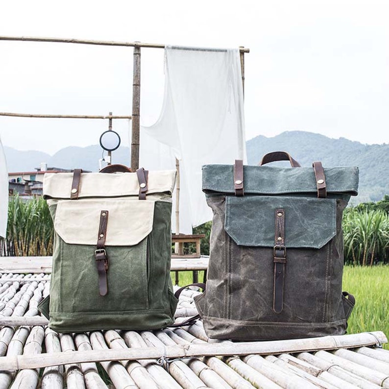 May include: Two canvas backpacks with leather straps and buckles. One backpack is green and the other is brown. Both backpacks have a flap closure.