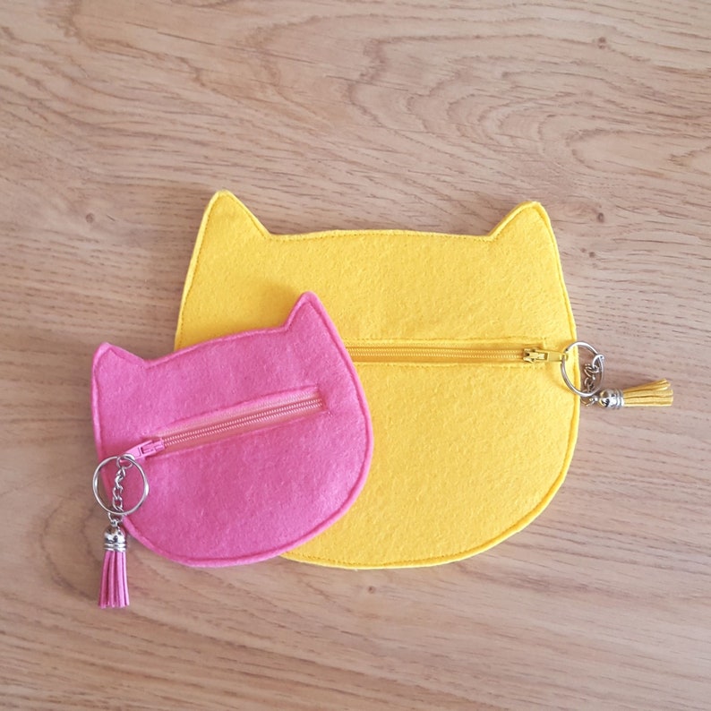 May include: Two felt cat-shaped coin purses, one pink and one yellow, with zippers and keychains.