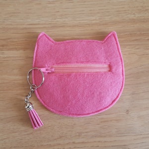 May include: A pink felt cat-shaped coin purse with a zipper closure and a silver key chain with a pink tassel.