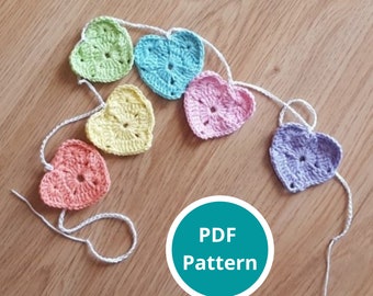 Könnte beinhalten: Eine Girlande aus gehäkelten Herzen in Pastellfarben, darunter rosa, gelb, grün, blau und lila. Die Herzen sind durch eine weiße Schnur verbunden. Das Bild enthält den Text "PDF Pattern".