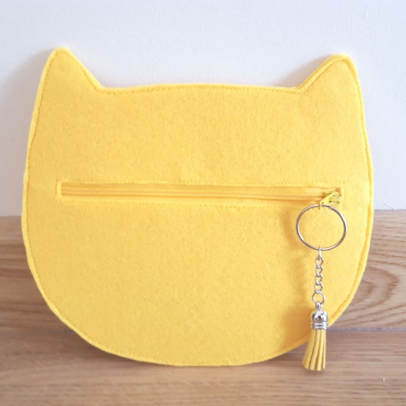 May include: A yellow felt cat-shaped pouch with a zipper closure and a silver key chain with a tassel.