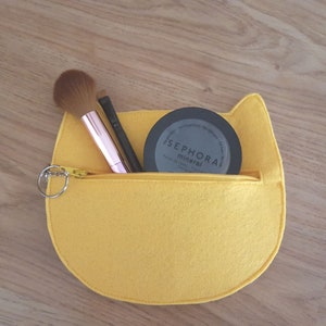 May include: Yellow felt cat-shaped makeup bag with a zipper closure. The bag is open and contains a black makeup compact with the text "SEPHORA mineral" and two makeup brushes.