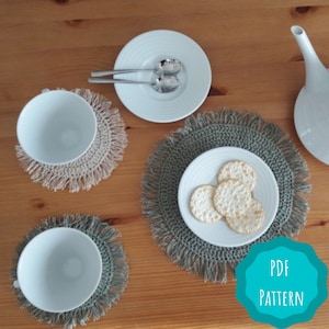 May include: Three crocheted coasters with fringe, two in beige and one in green, with a white plate and crackers on top of one of the green coasters. The text "PDF PATTERN" is on a teal circle.