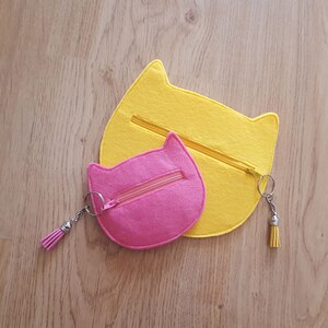 May include: Two felt cat-shaped zipper pouches, one yellow and one pink. The pouches have a zipper closure and a small tassel attached to the zipper pull.