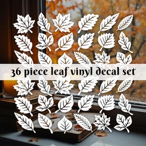 May include: A collection of 36 white leaf vinyl decals in various shapes and sizes. The decals are arranged on a window sill with books and a candle, with a blurred autumn background visible through the window.