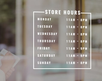 May include: A glass storefront displays store hours in white text. The hours are listed for each day of the week, with opening and closing times. A person is visible in the background, holding a notepad and pen.