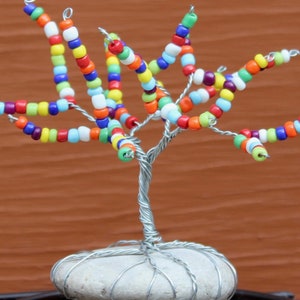Pode incluir: Uma escultura de &aacute;rvore de arame com contas coloridas e uma base de pedra branca. As contas s&atilde;o dispostas em espiral nos ramos, criando um design vibrante e caprichoso.