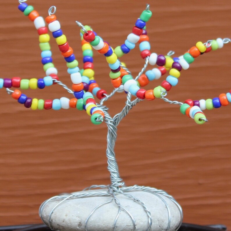 Pode incluir: Uma escultura de &aacute;rvore de arame com contas coloridas e uma base de pedra branca. As contas s&atilde;o dispostas em espiral nos ramos, criando um design vibrante e caprichoso.