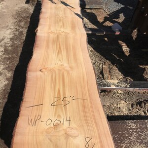 May include: A light brown wood slab with a natural edge. The slab is 25 inches wide and 12 8/4 inches long. The wood is marked with the text "WP-0014".